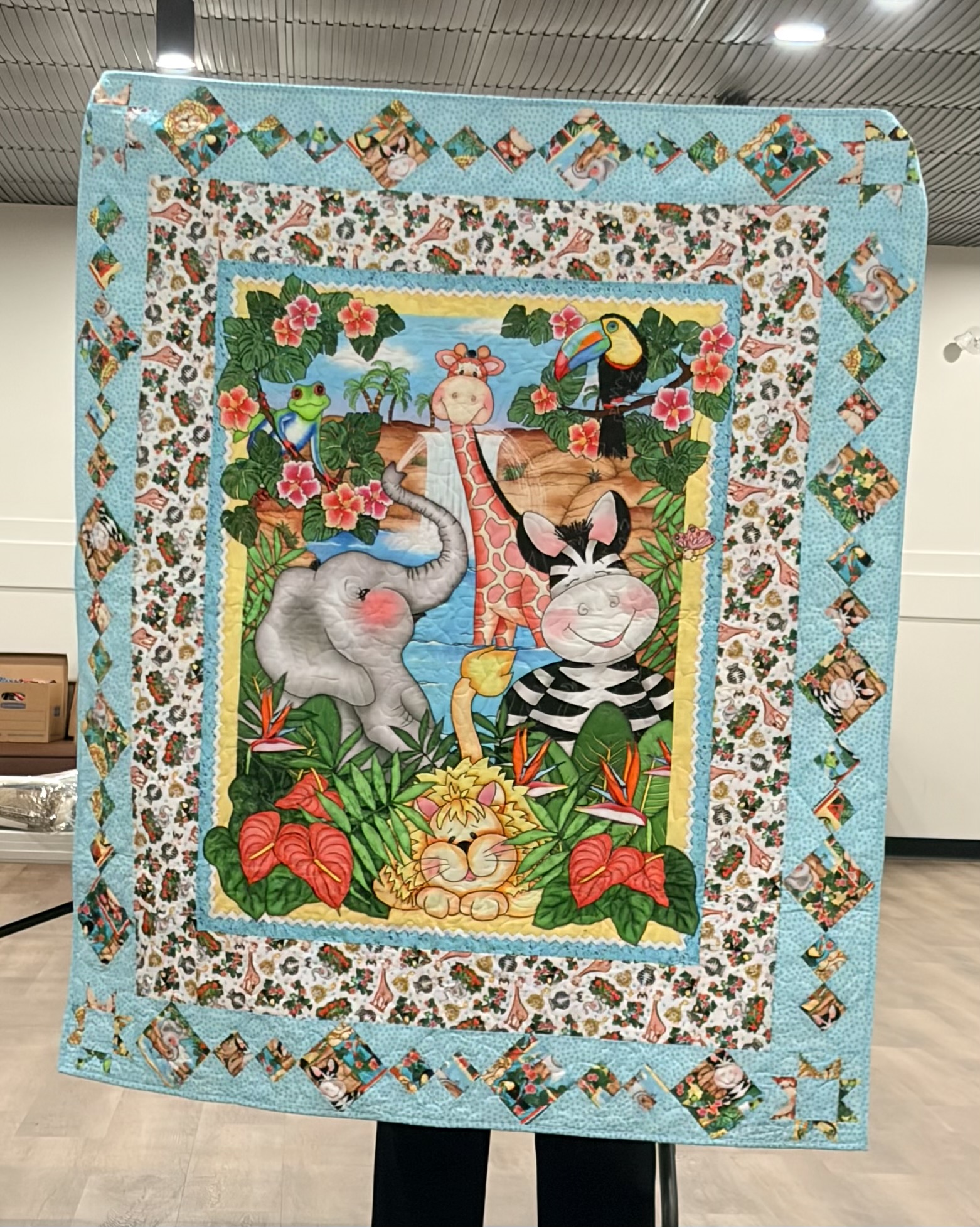 Jungle animals panel quilt with a smiling elephant, giraffe, zebra, and lion framed by blue borders