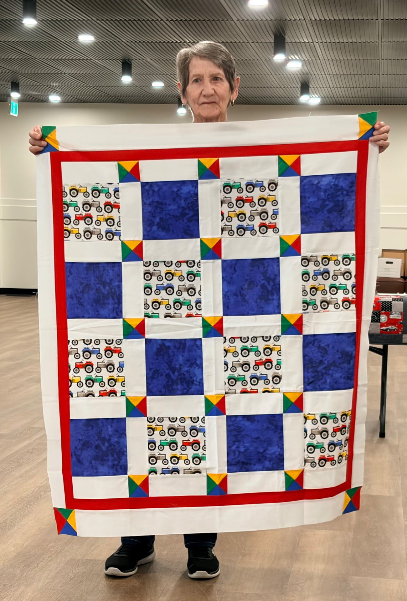 Tractor-print nine-patch baby quilt in red, white, and blue with corner triangle accents
