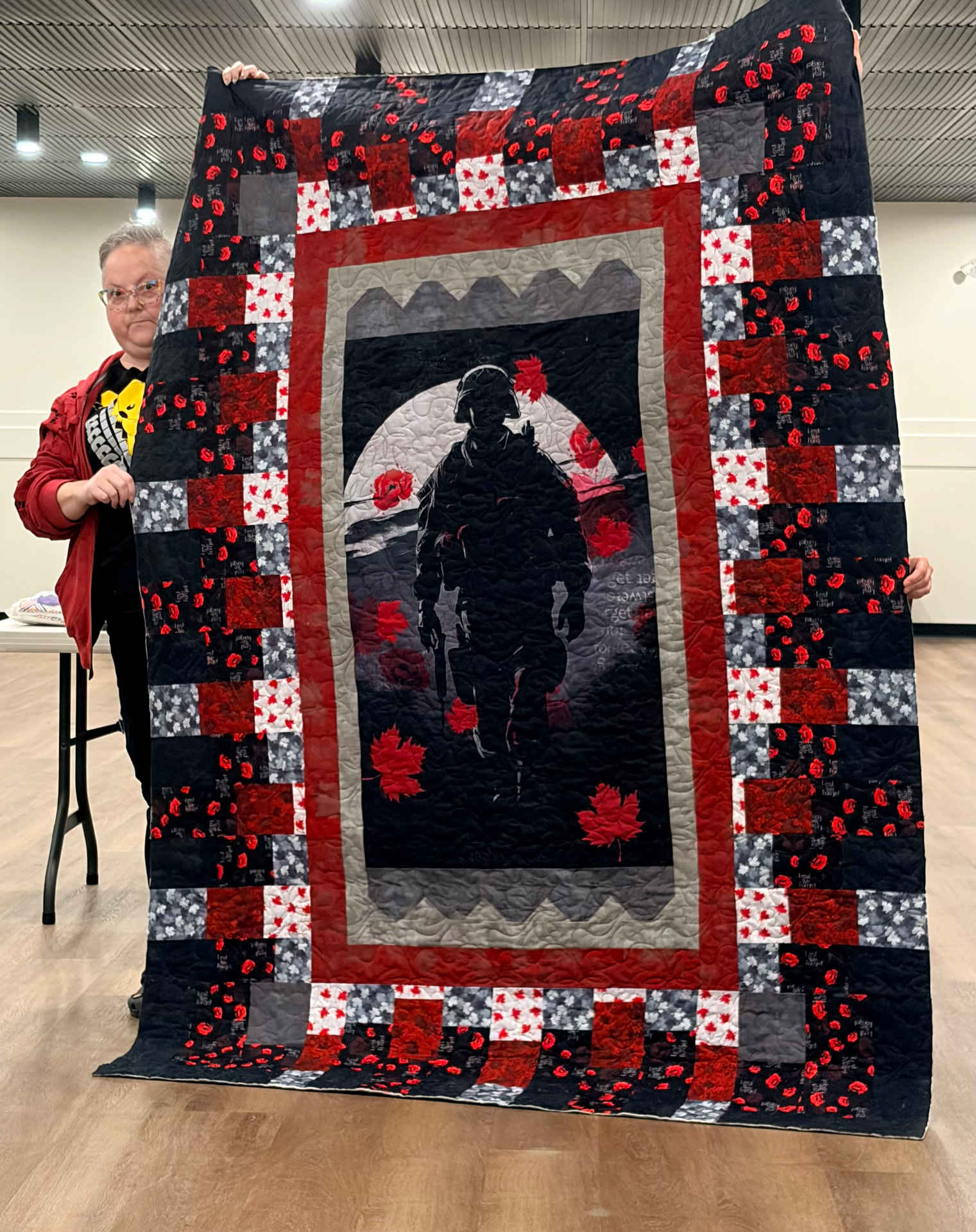 Remembrance quilt with a soldier panel framed by red poppy prints and black borders