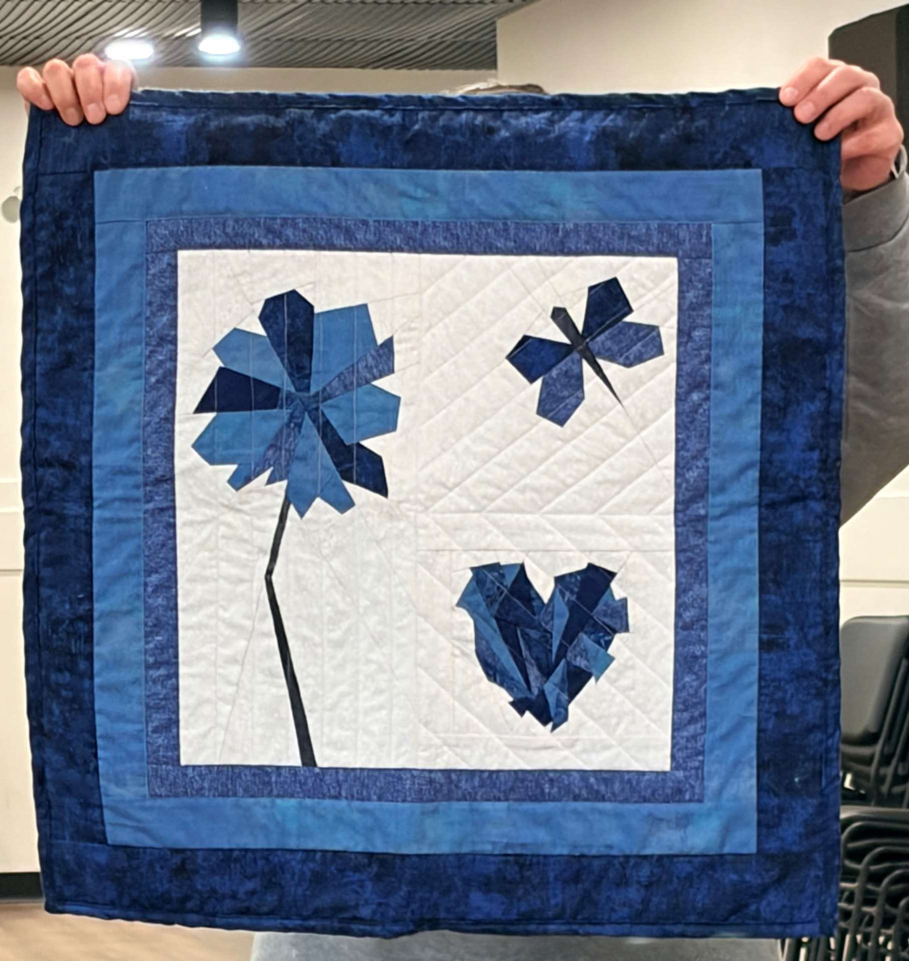 Blue and white quilt with a dandelion flower, dragonfly, and crumpled paper heart