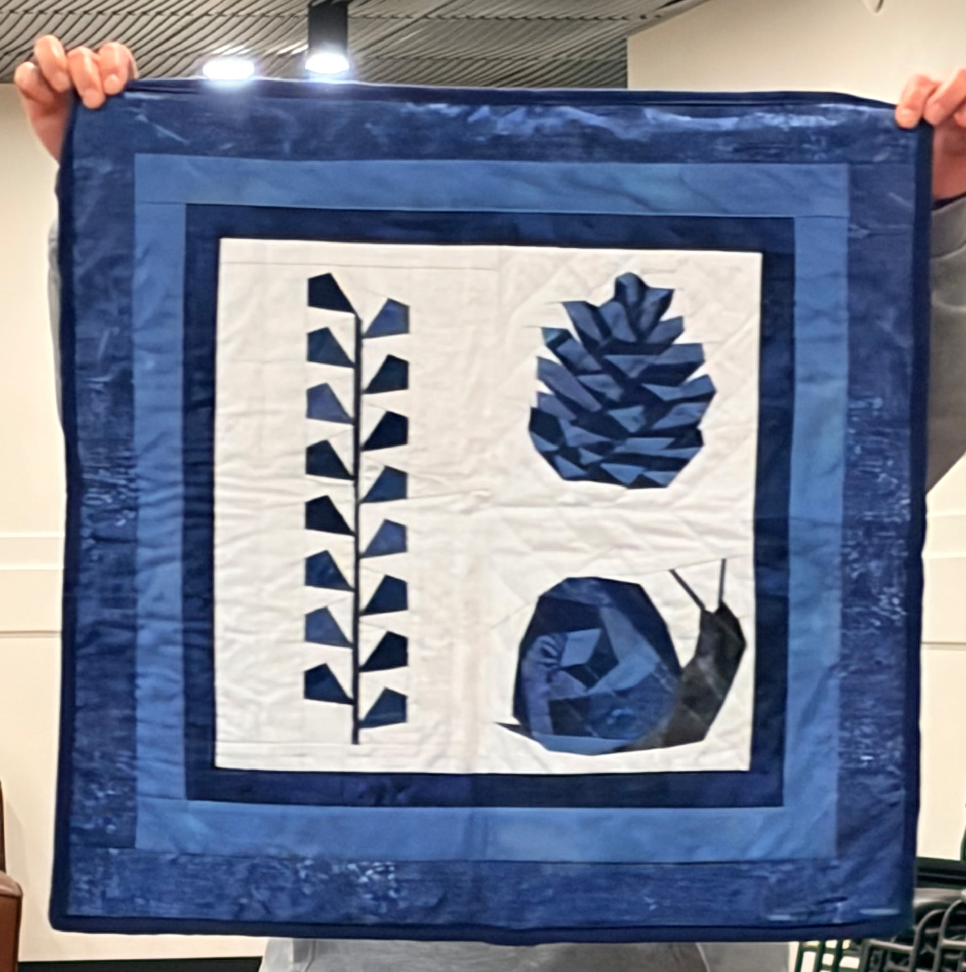 Blue and white quilt with a pinecone, snail, and leaf vine