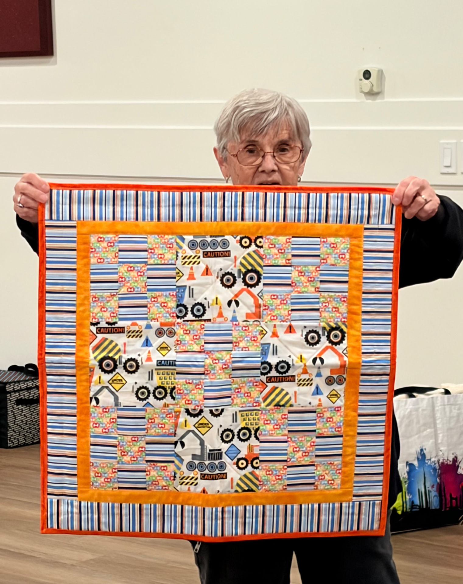 Construction-truck baby quilt with orange border and striped frame